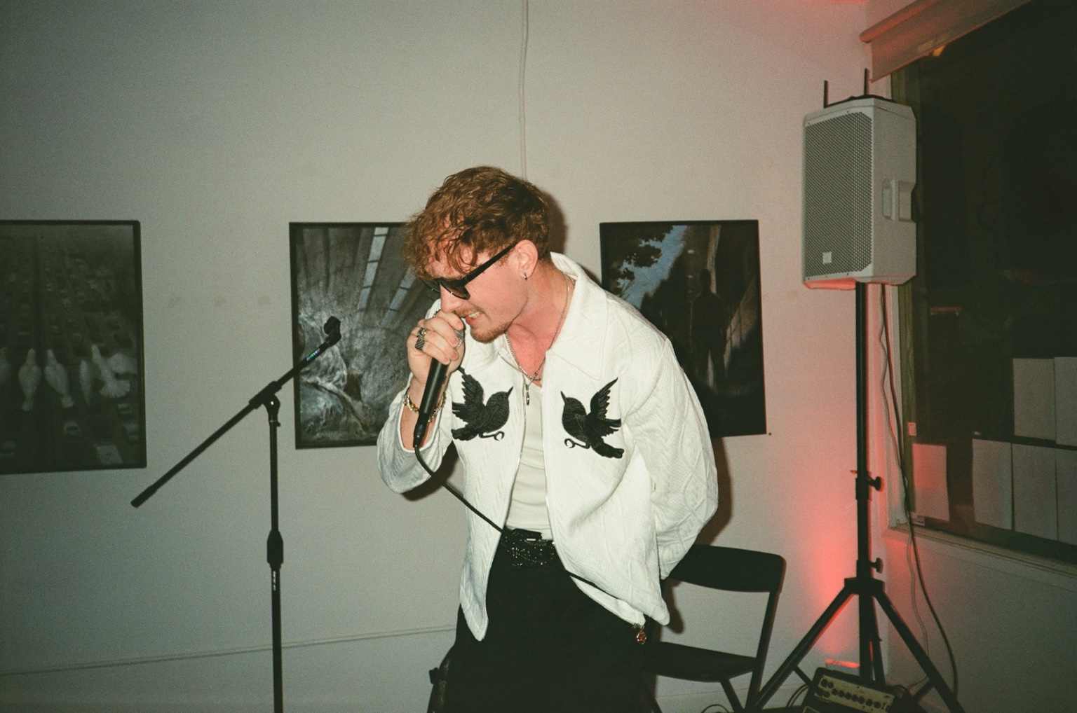 ProllyRed performing with a microphone in a white bird-embroidered jacket
