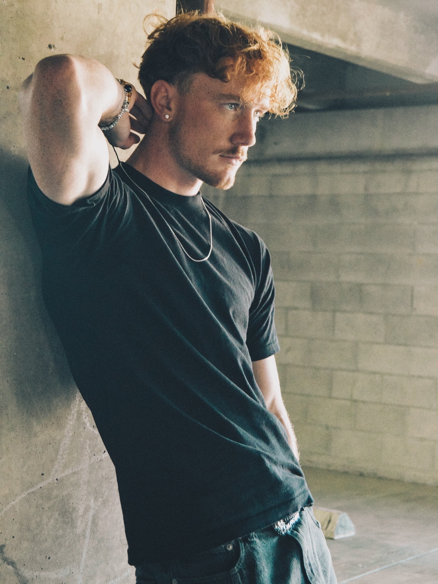 ProllyRed in a black shirt leaning against a concrete wall
